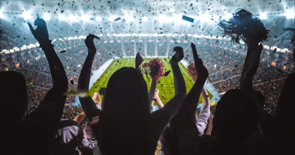 Group of fans cheer facing a football field